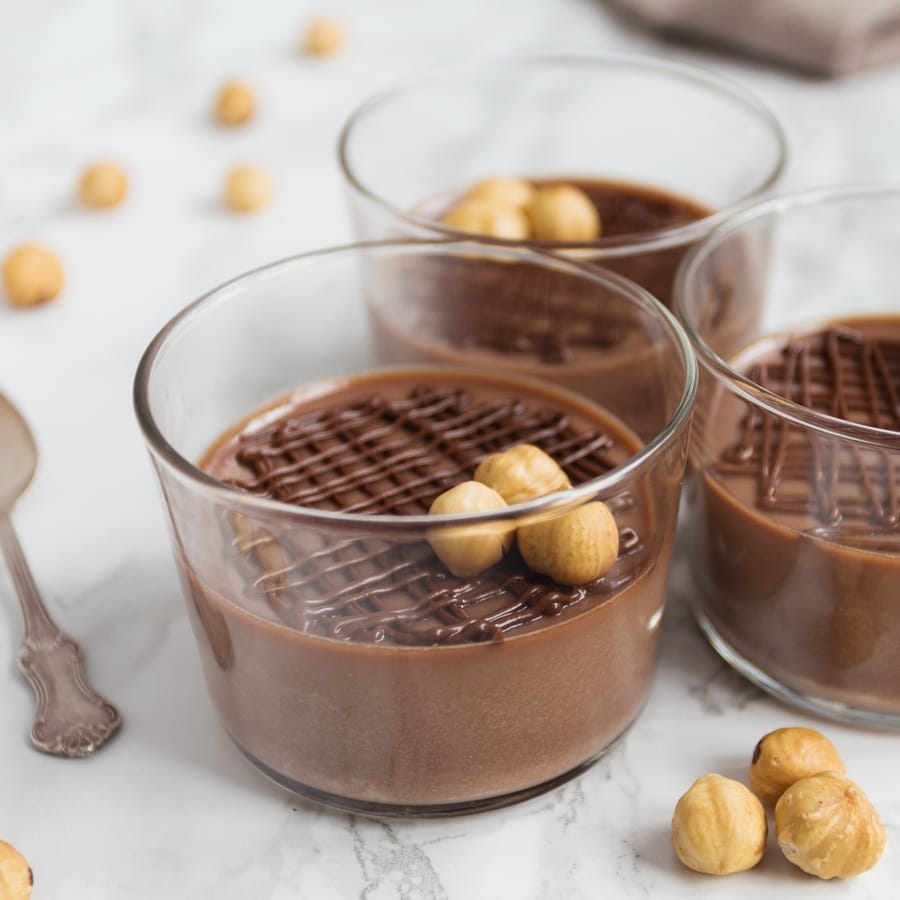 Nutella panna cotta served in see-through glasses and decorated with hazelnuts.