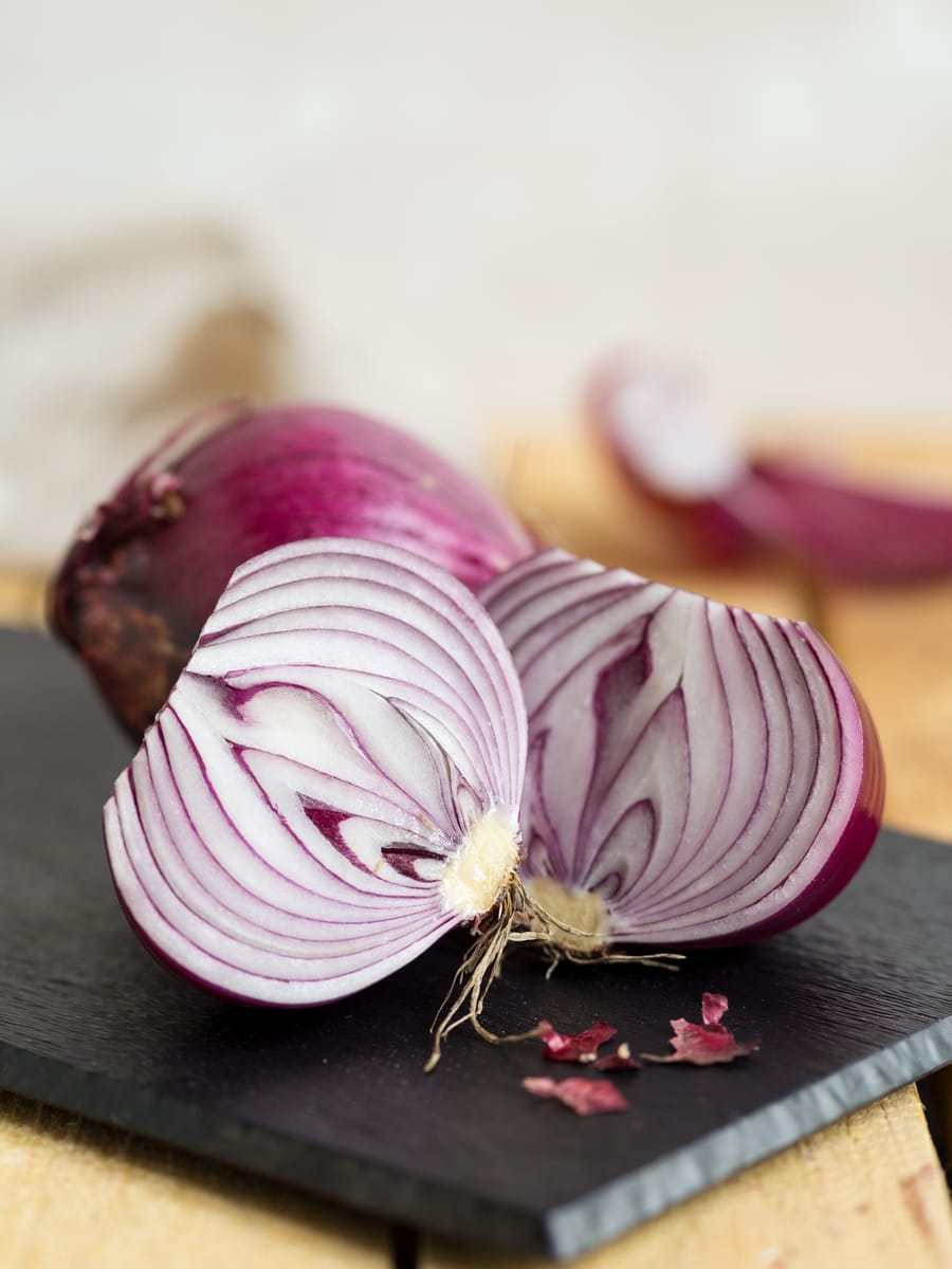 Two onions on a cutting board, one is cut in half.