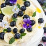 Australian cake pavlova with mango cream, blueberries, banana slices, pansies, mint leaves and lime curd drizzle.