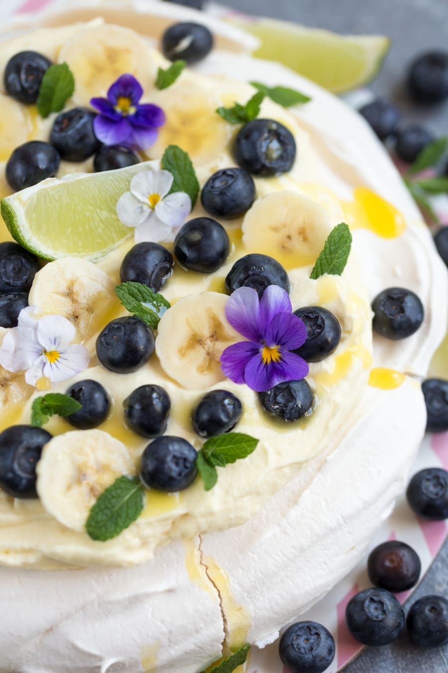 Australian cake pavlova with mango cream, blueberries, banana slices, pansies, mint leaves and lime curd drizzle.
