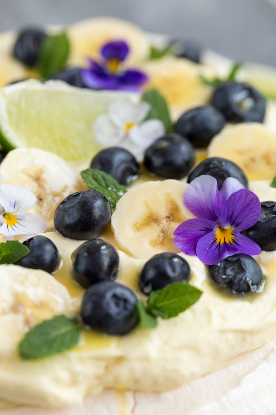Australian cake pavlova with mango cream, blueberries, banana slices, pansies, mint leaves and lime curd drizzle.