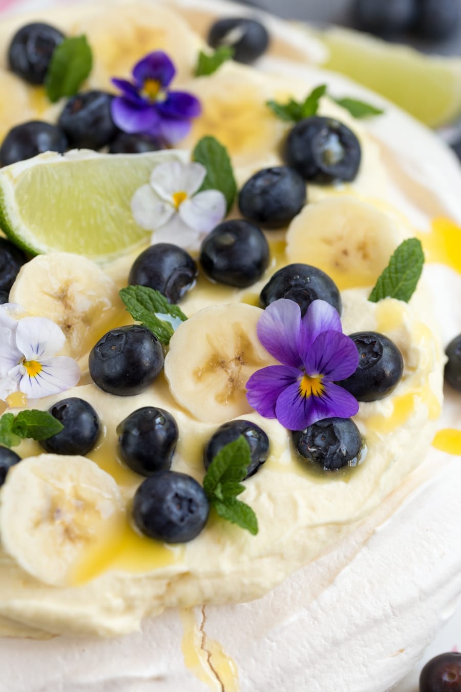 Australian cake pavlova with mango cream, blueberries, banana slices, pansies, mint leaves and lime curd drizzle.