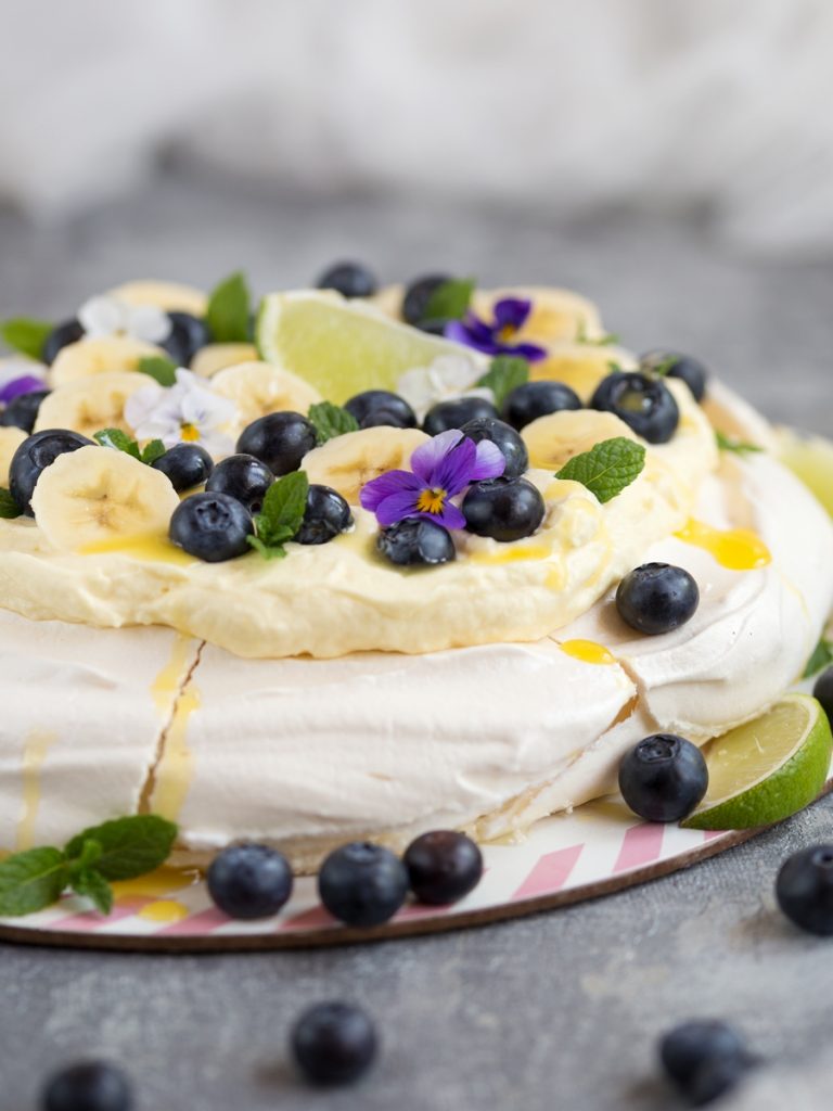 Australian cake pavlova with mango cream, blueberries, banana slices, pansies, mint leaves and lime curd drizzle.