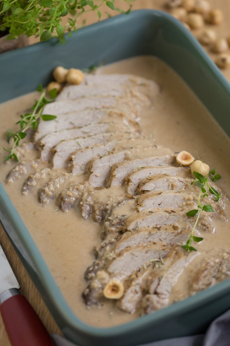 Baked pork loin in hazelnut sauce in green casserole dish.
