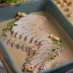 Baked pork loin in hazelnut sauce in green casserole dish.