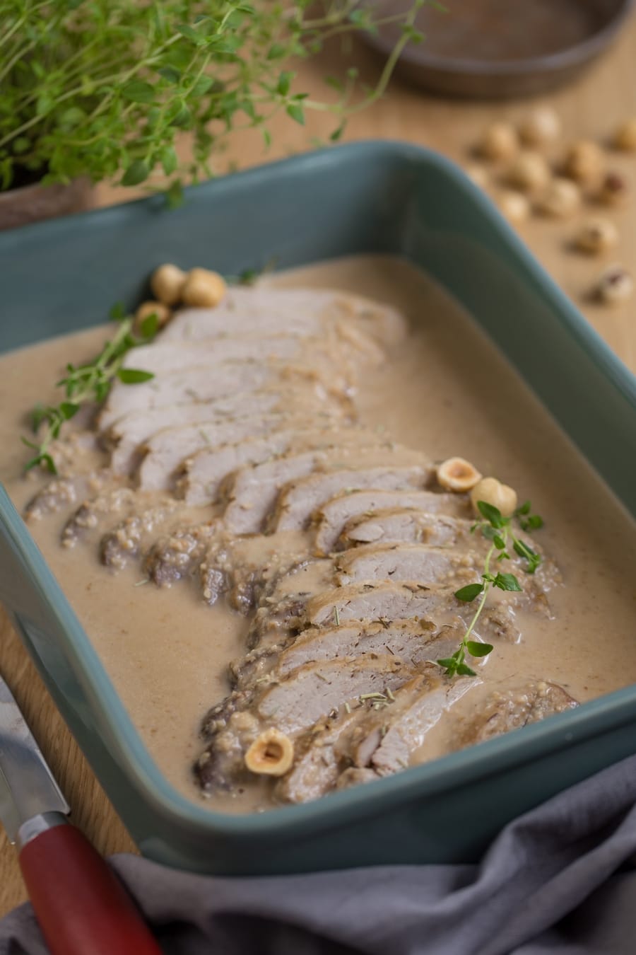 Baked pork loin in hazelnut sauce in green casserole dish.