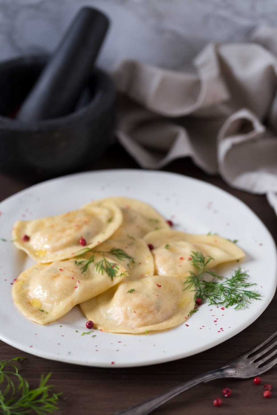 Smoked salmon ravioli with dill and pink peppercorns on a white plate.