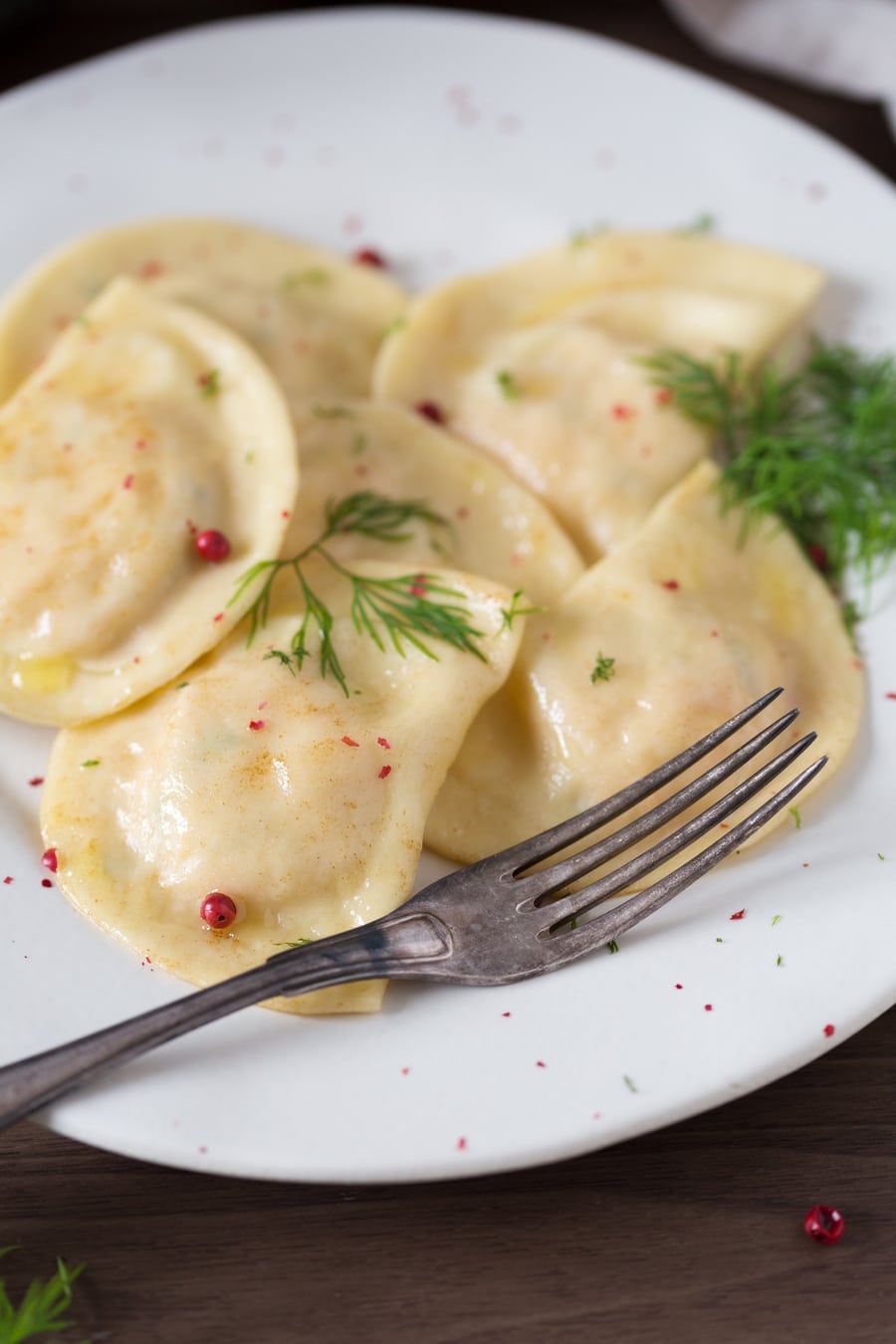 Smoked salmon ravioli with dill and pink peppercorns on a white plate.