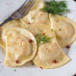 Smoked salmon ravioli with dill and pink peppercorns on a white plate.