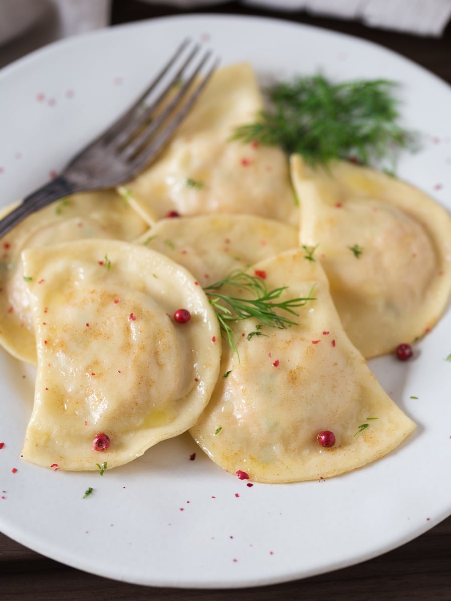 Smoked salmon ravioli with dill and pink peppercorns on a white plate.