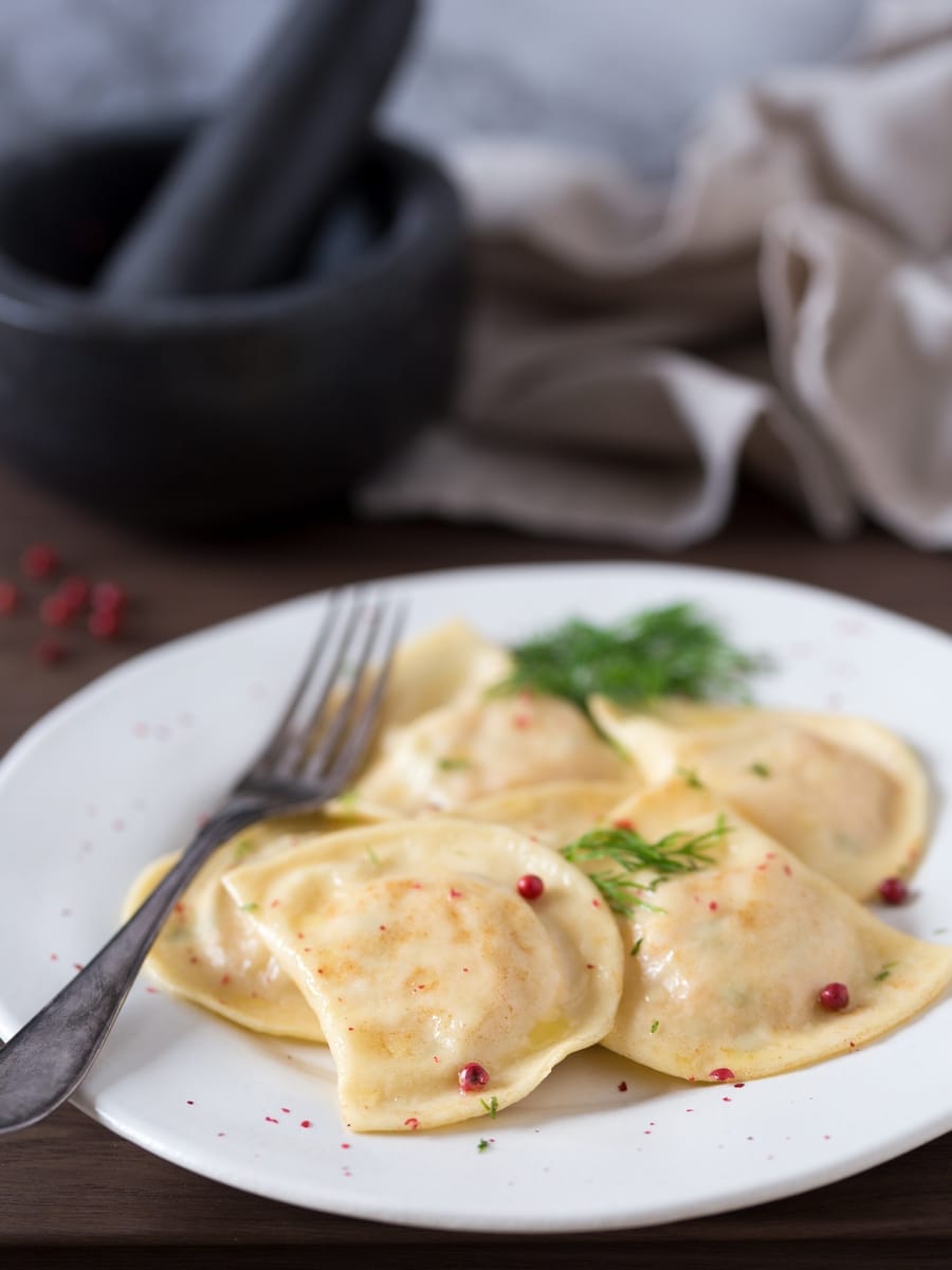Smoked salmon ravioli with dill and pink peppercorns on a white plate.