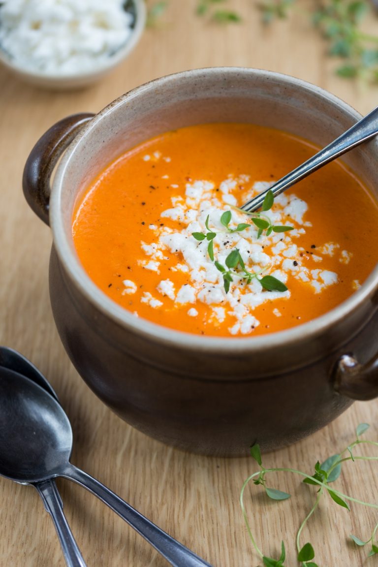 Orange pepper soup and white cheese crumbs in a brown clay pot, ladle in soup.