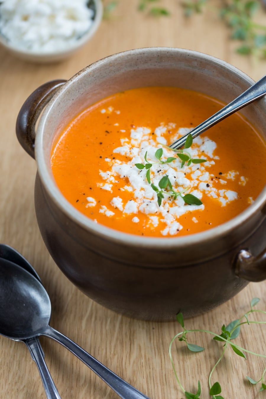 Orange pepper soup and white cheese crumbs in a brown clay pot, ladle in soup.