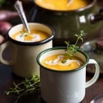 Roasted pumpkin and red lentil soup in enamel mugs, decorated with fresh thyme.