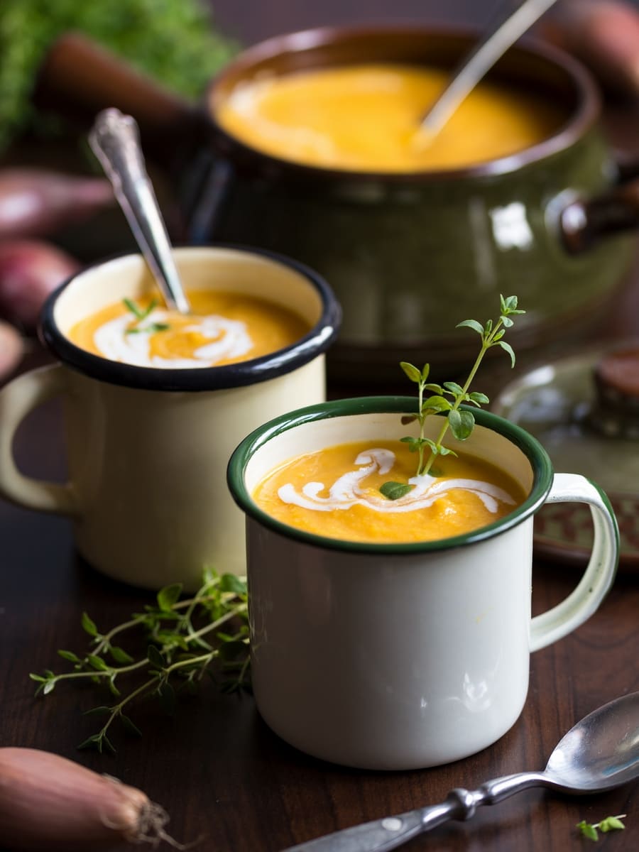 Roasted pumpkin and red lentil soup in enamel mugs, decorated with fresh thyme.
