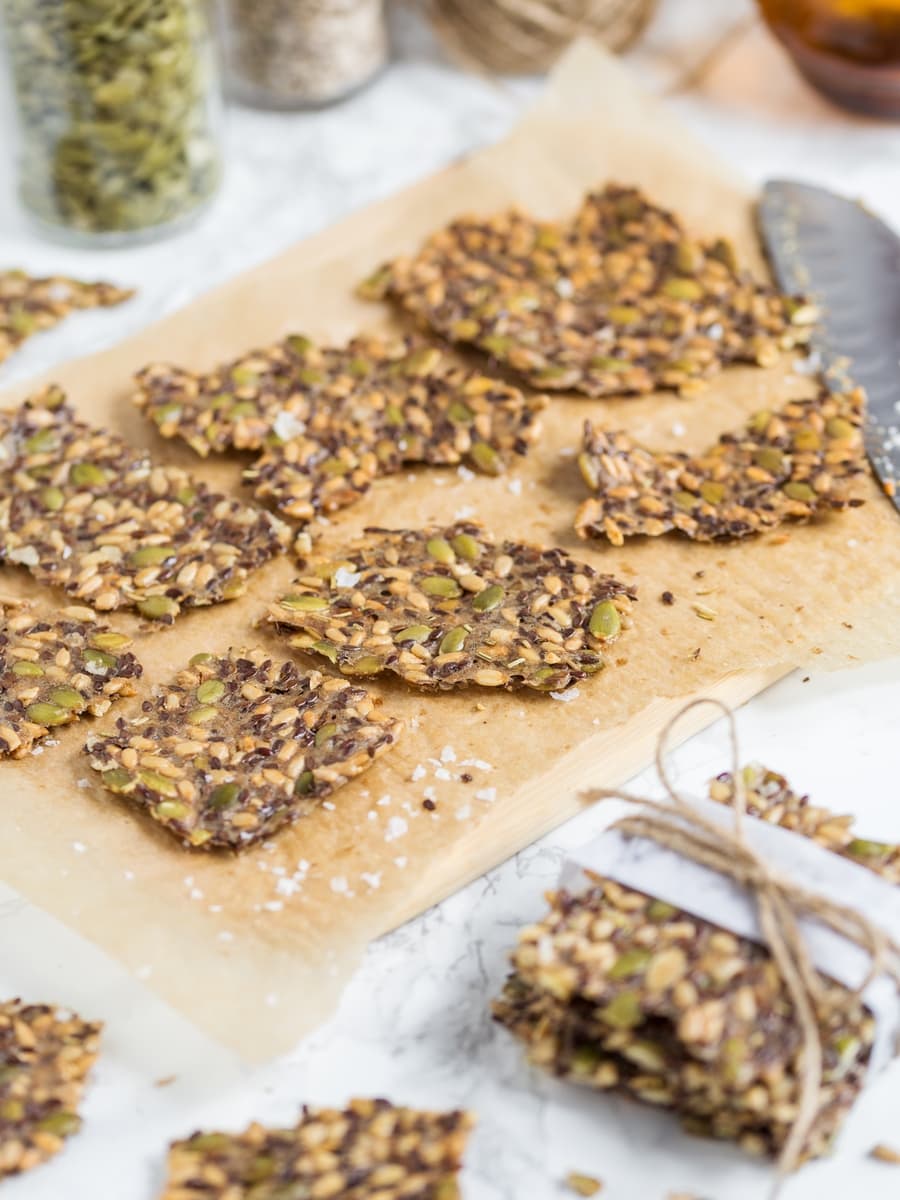 Seed crackers on a cutting board, knife on the right, seed jars in the background.