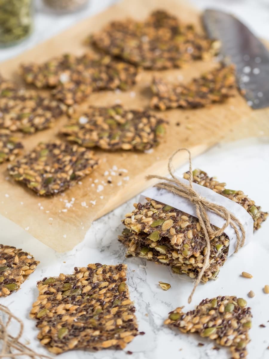 Stacked seed crackers wrapped and tied, seed crackers on cutting board in the background.