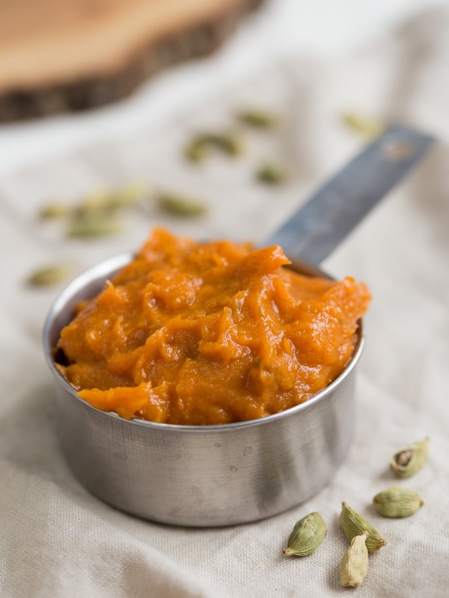 Roasted sweet potato mash in a half cup, cardamom pods around it.