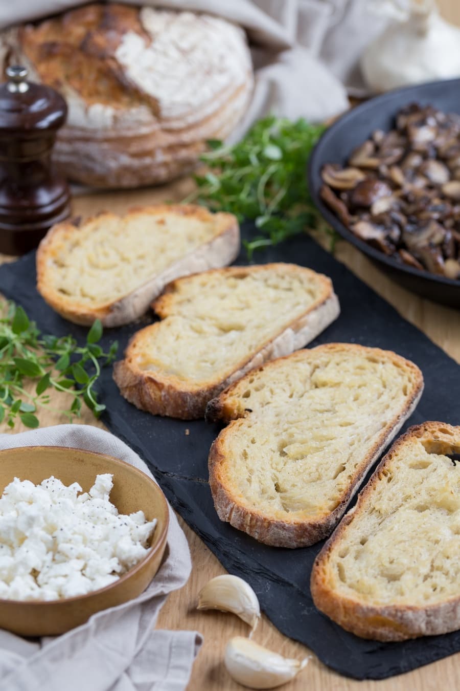 Ingredients to mushroom crostini around toasted bread slices on cutting board.