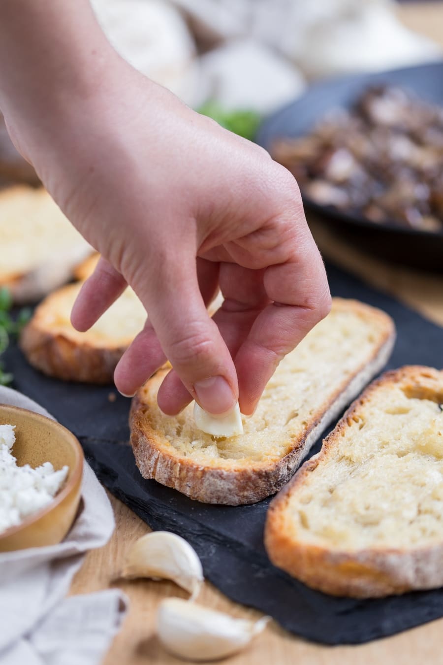 Hand smearing fresh garlic clove on toasted bread.