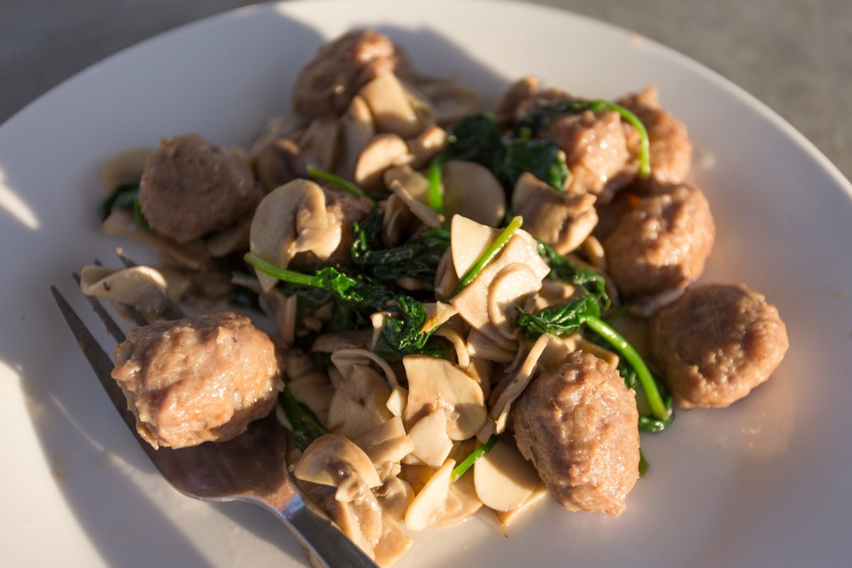 Cooked sauseage balls with mushrooms and spinach.