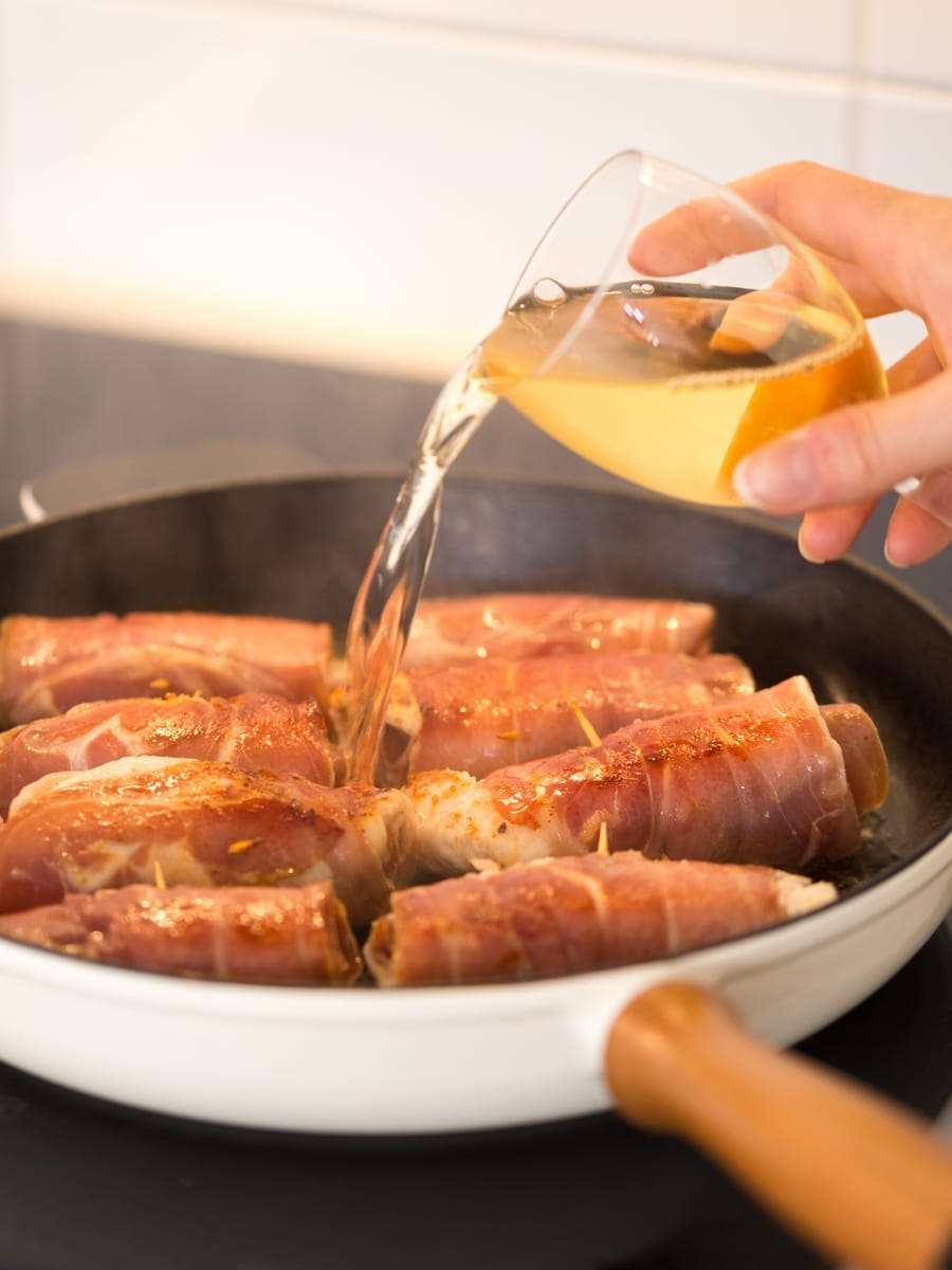 Adding white wine to cooking chicken involtini in cast iron skillet.