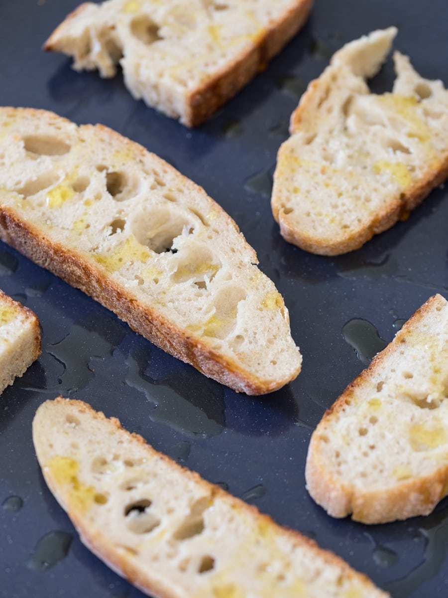 Sourdough bread slices drizzled with olive oil on an oven tray.