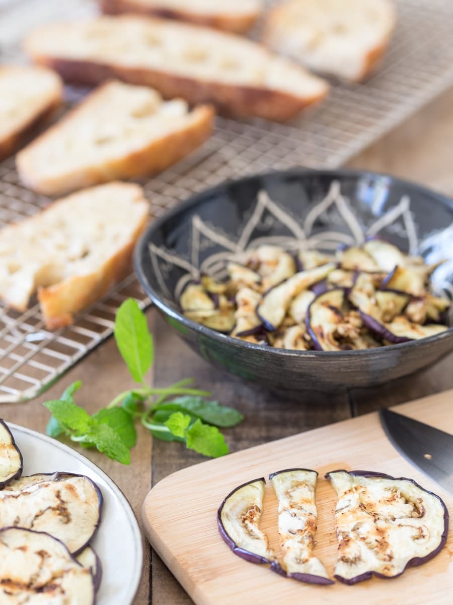 Grilled eggplant sliced being cut and added to a black bowl.