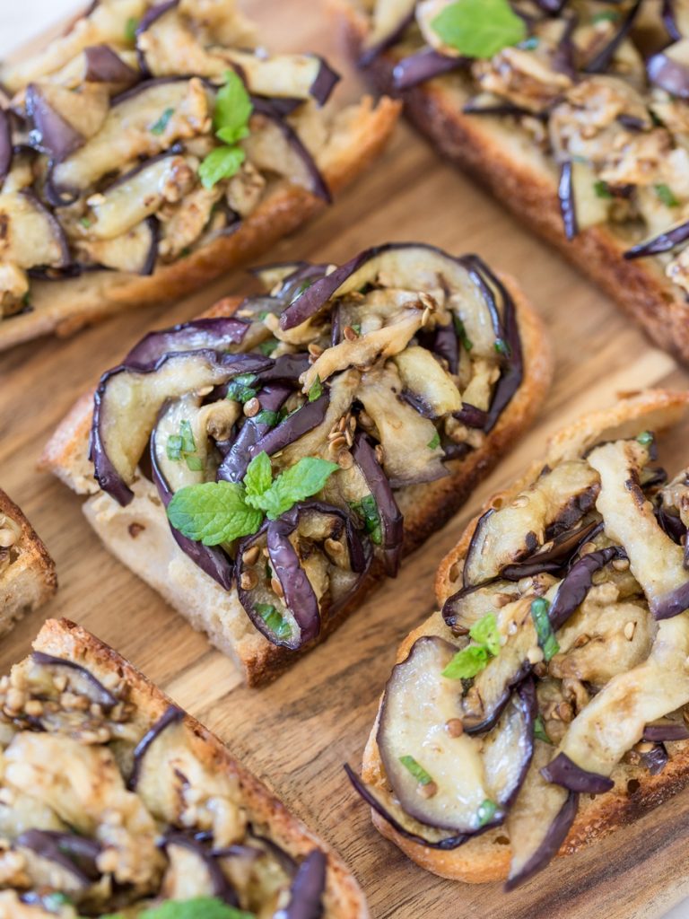 Closeup of grilled eggplant bruschetta with fresh mint leaves.