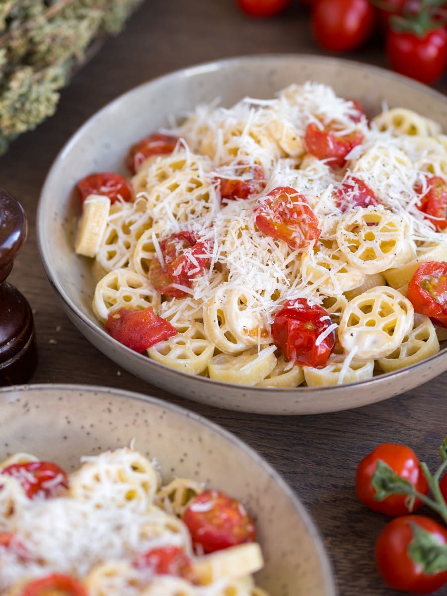 Two bowls of roasted cherry tomato pasta in beige serving bowls.