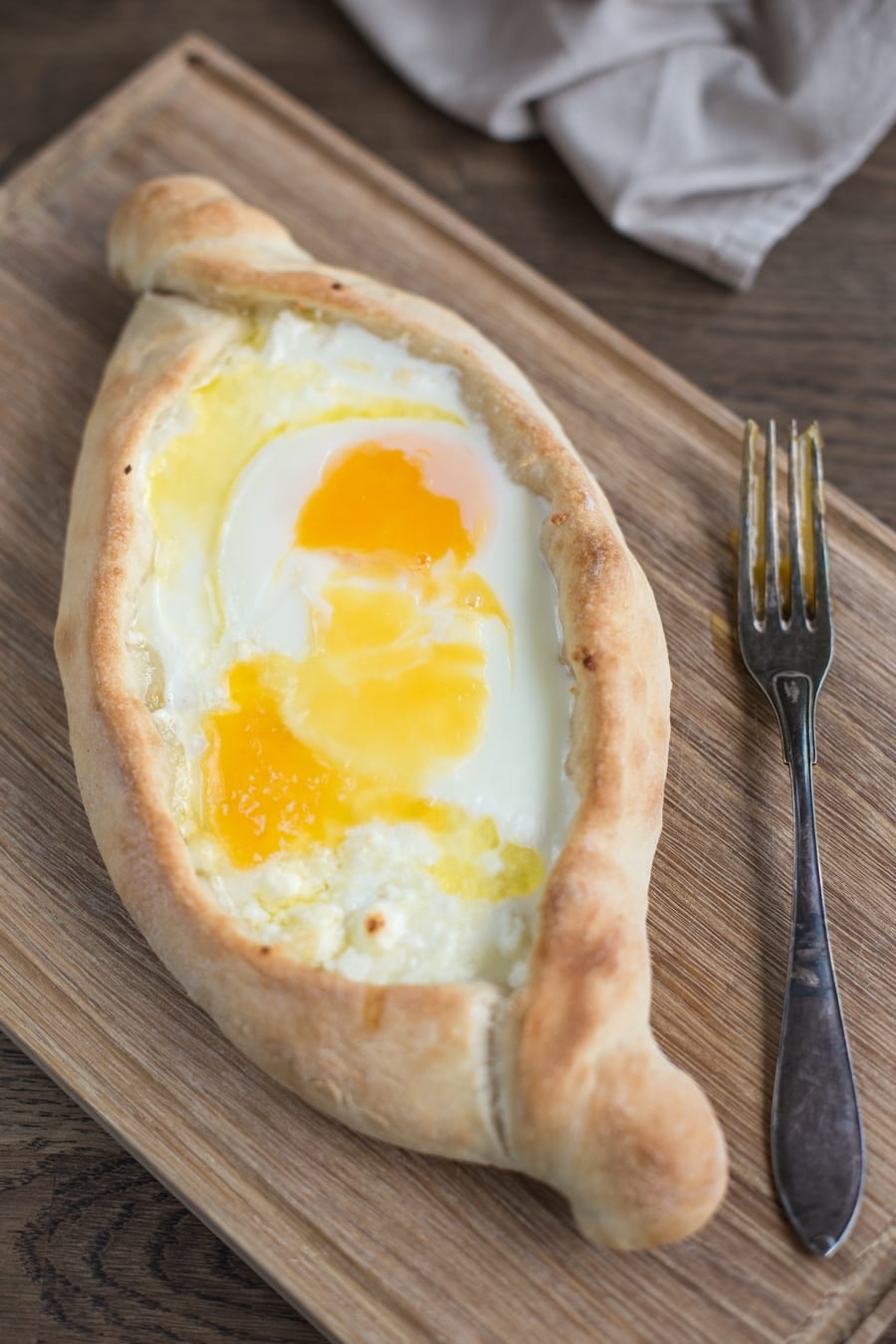 Sourdough khachapuri adjaruli on wooden board.