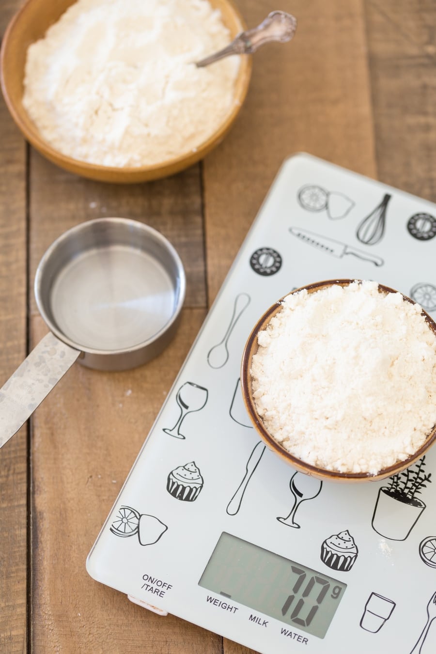 A bowl of flour on a kitchen scale, a measuring cup with water on the side.