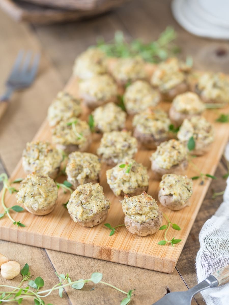 Baked stuffed mushrooms with a cream cheese and hazelnut filling served on a wooden tray.