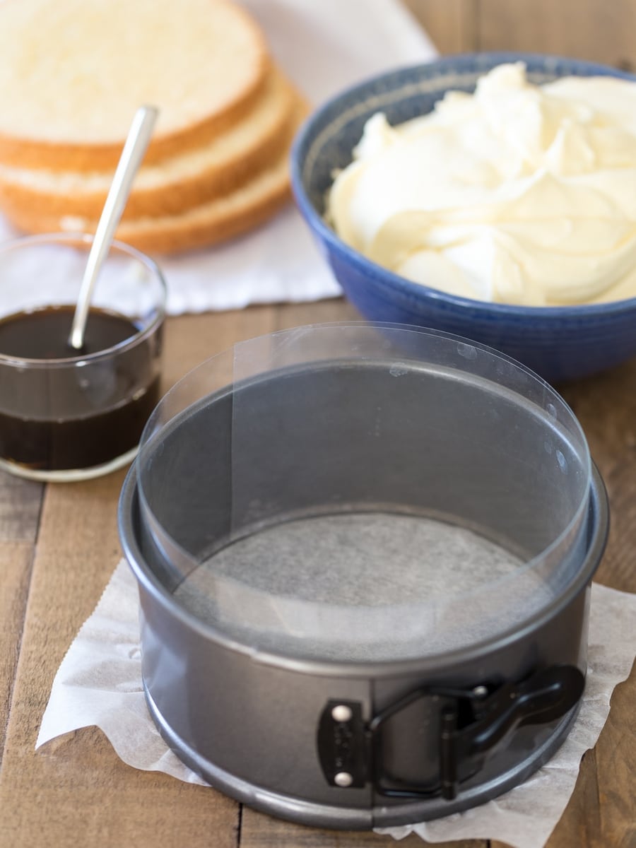 Cake pan lined with cake collar; tiramisu ingredients around it.
