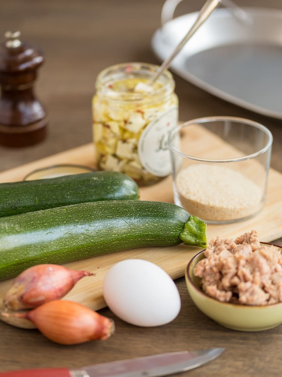 Ingredients needed fot tuna stuffed zucchini boats placed on a wooden tray and around.