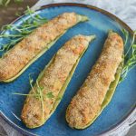 Tuna stuffed zucchini boats served on a blue plate with pea shoots as decoration.
