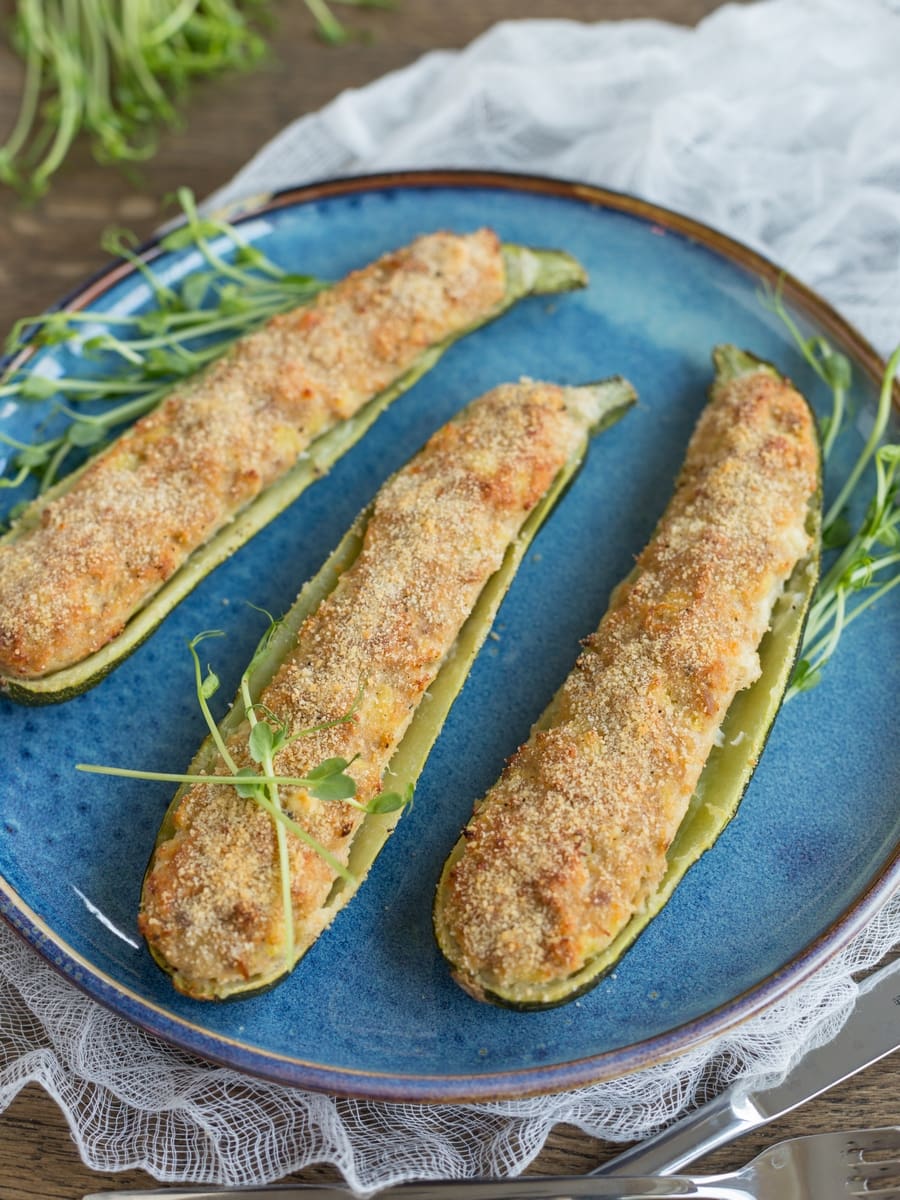 Tuna zucchini boats served on a blue plate with pea shoots as decoration.
