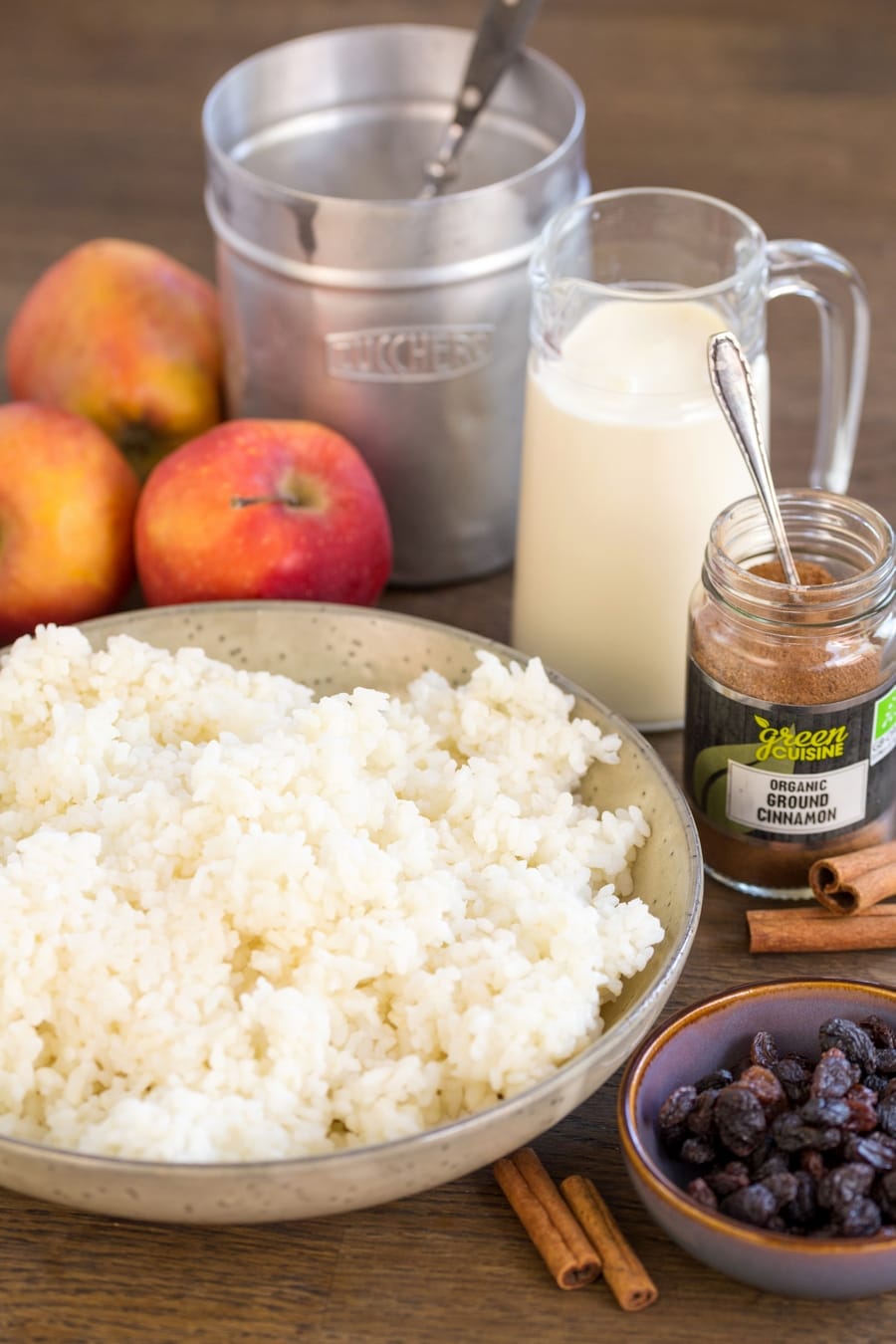 Cooked rice in a bowl, raisins, ground cinnamon, whipping cream, sugar and apples: the ingrdients needed to make baked rice with apples.