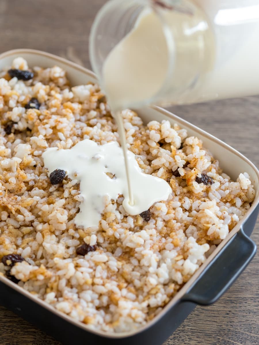 Pouring whipping cream over rice apple casserole.