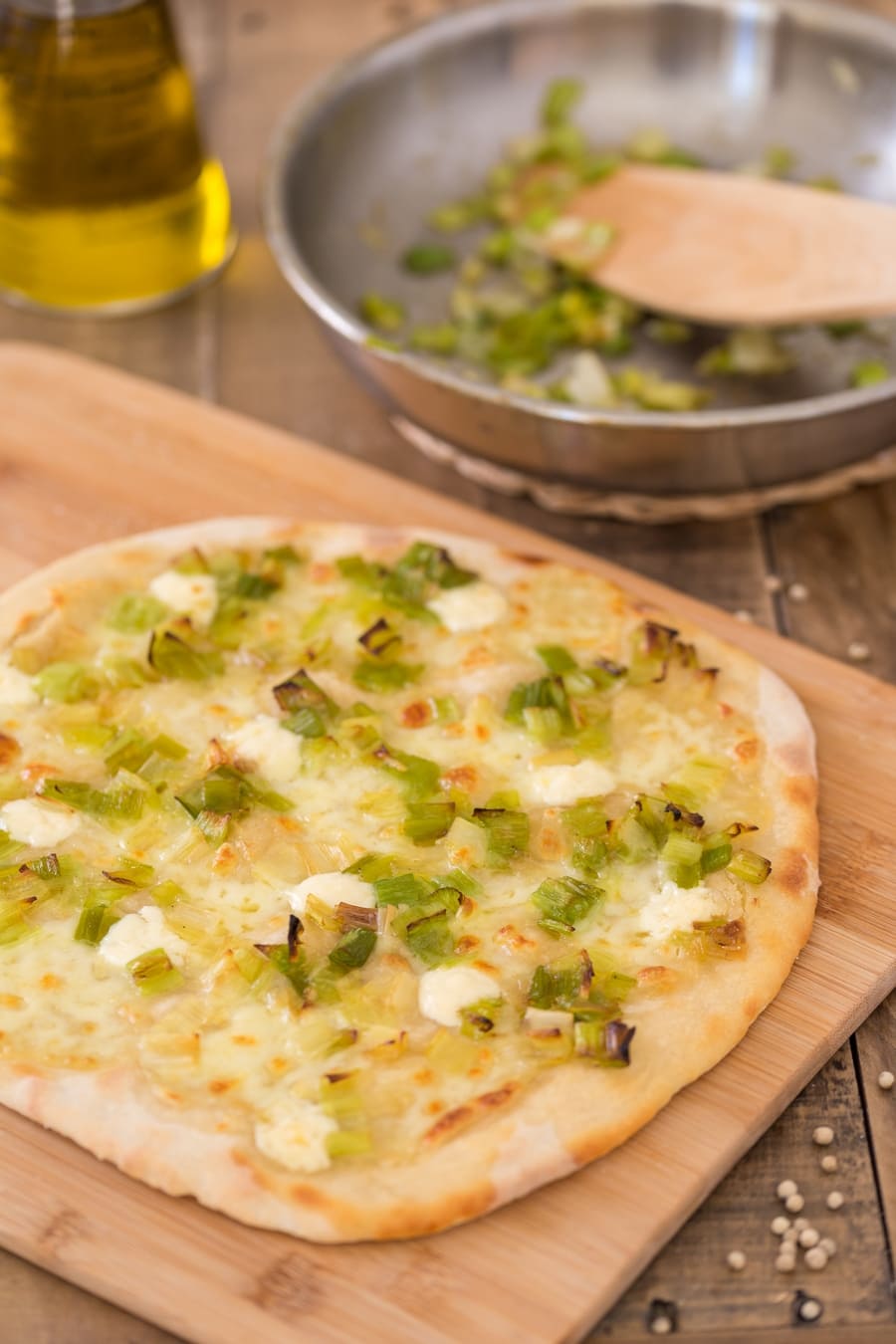 Stone-baked leek mascarpone pizza bianca on a wooden board.