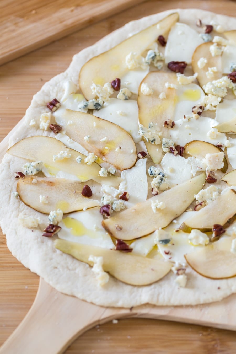 Uncooked pear blue cheese pizza with a nice drizzle of olive oil on top.