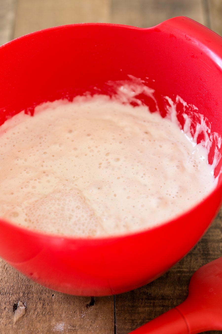 Red bowl containing mature poolish to be added to pizza dough.