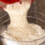Adding poolish to flour and water mix to make pizza dough.