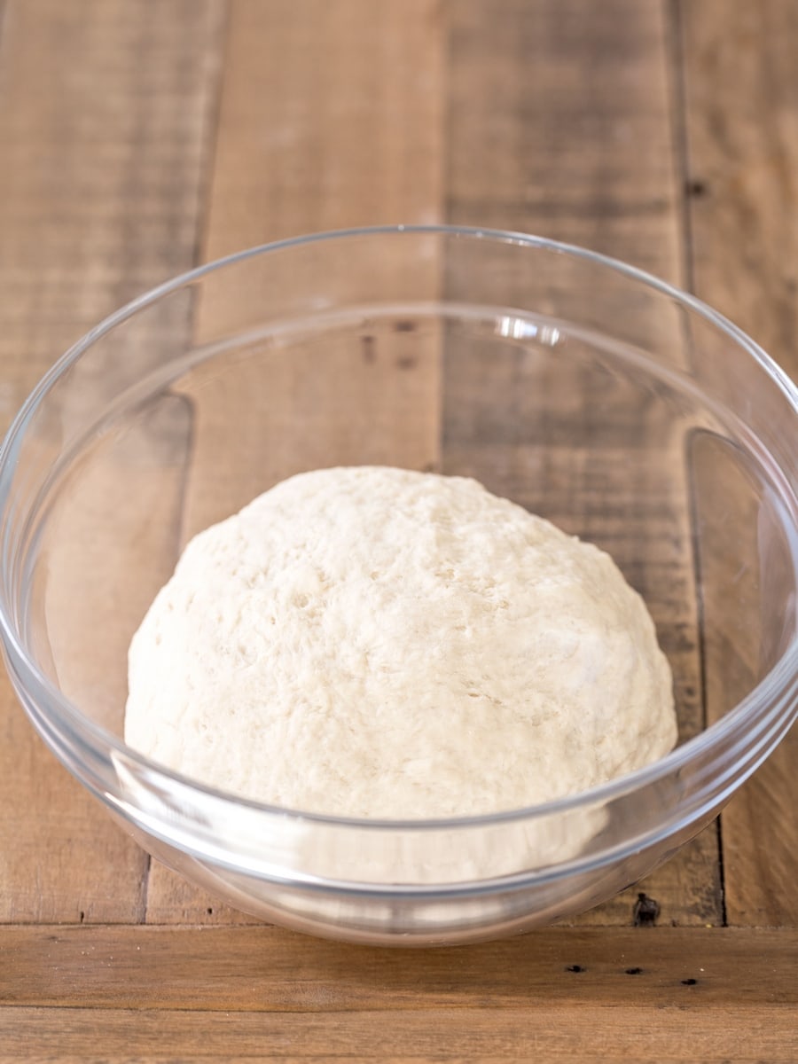 Poolish pizza dough resting in a glass bowl for bulk fermentation.
