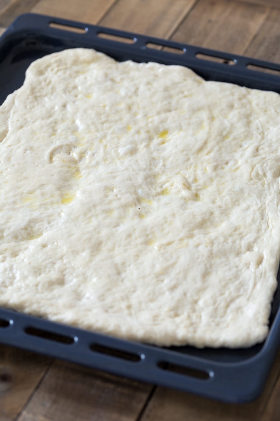 Pizza dough made with poolish. The dough gets stretched and is allowed to proof in the baking pan.