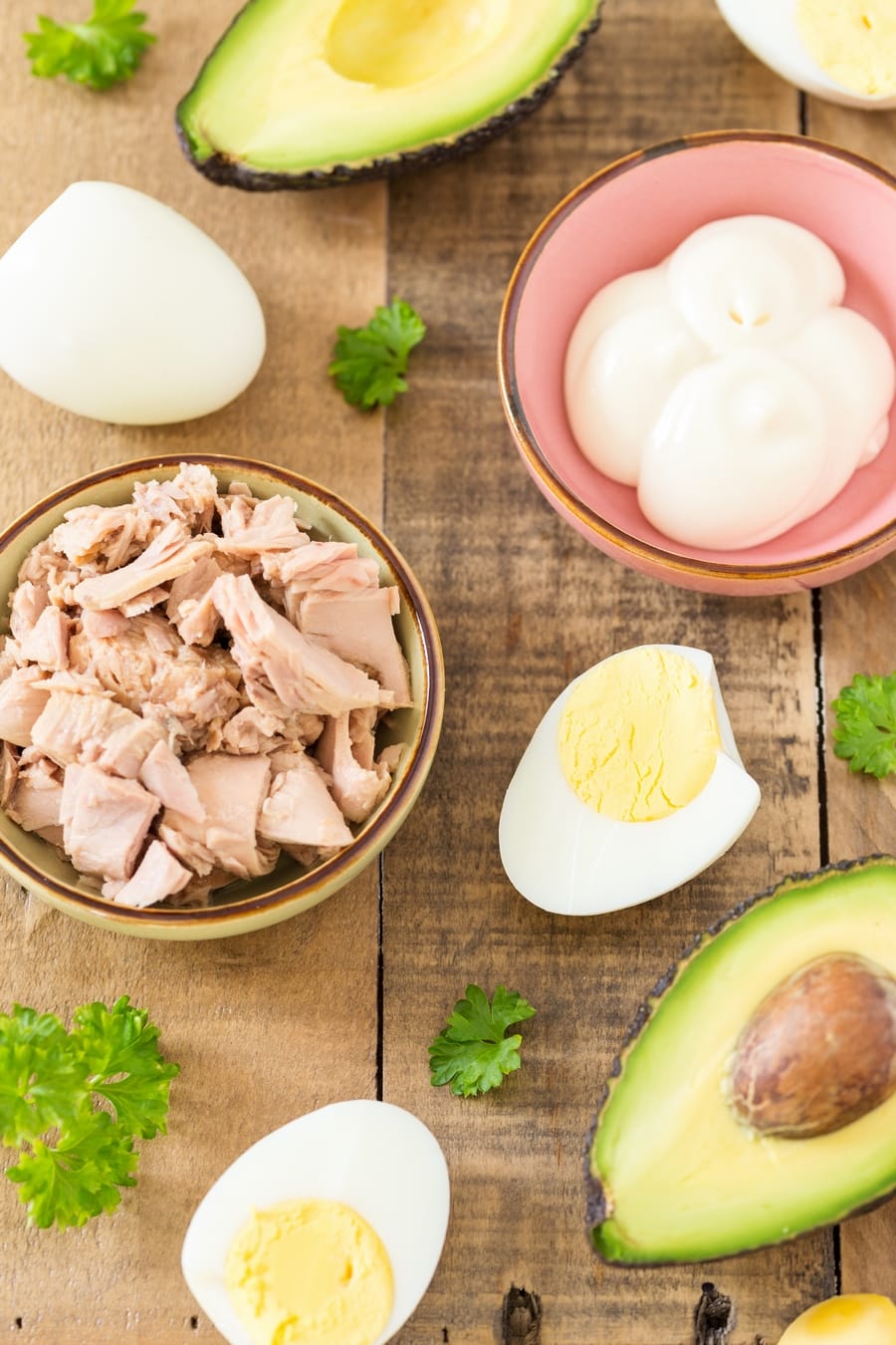 Tuna, avocado, boiled eggs, mayonnaise and parsley on a table.