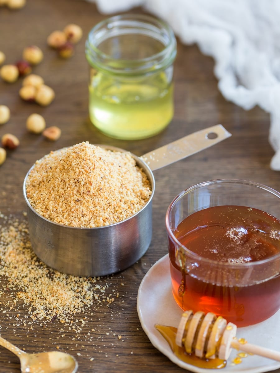 Hazelnut meal, liquid honey, egg whites in a jar and toasted hazelnuts.
