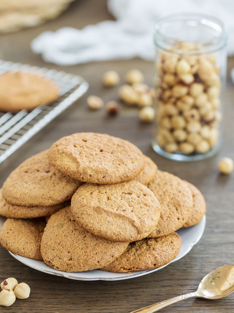 Honey hazelnut meringue cookies on a plate, toasted hazelnuts in a jar behind.