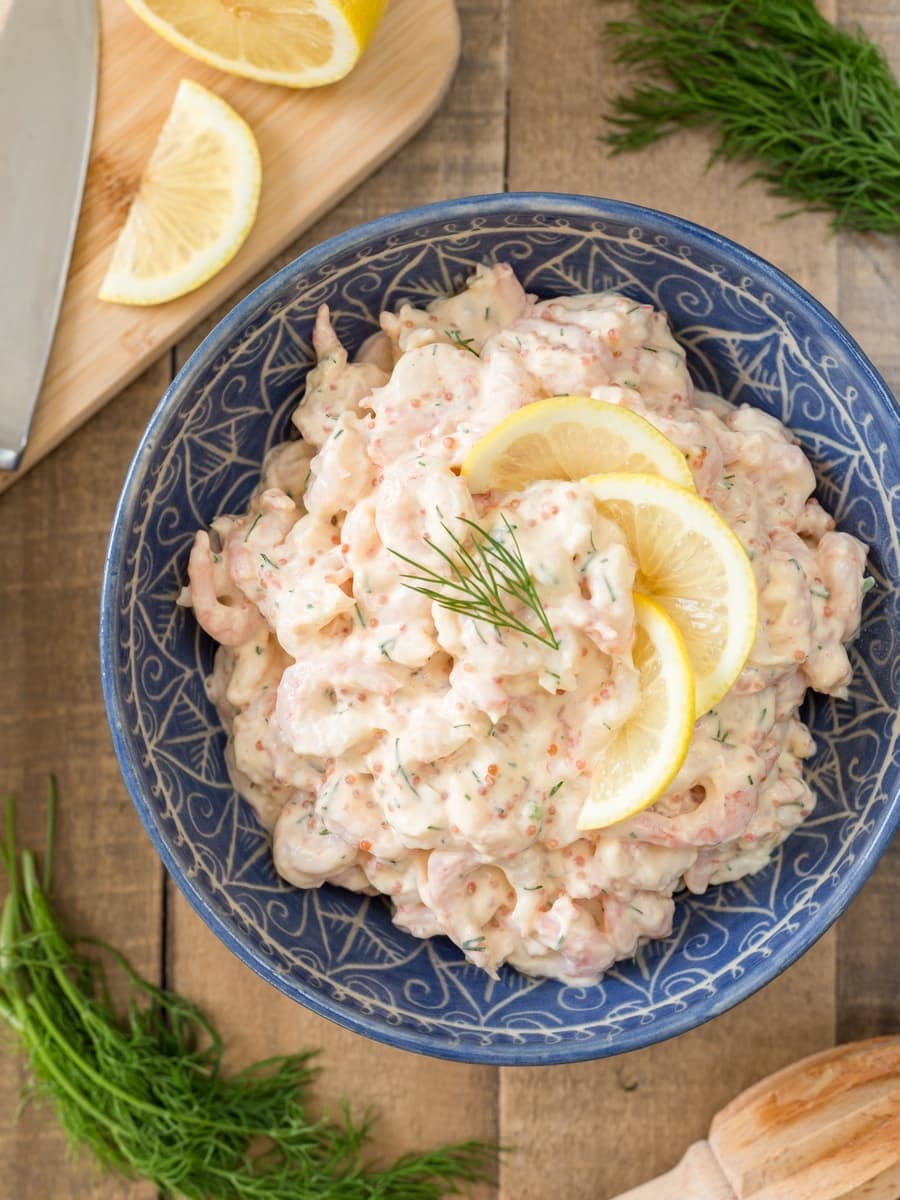 Swedish shrimp salad skagenröra in a blue bowl, garnished with lemon slices.