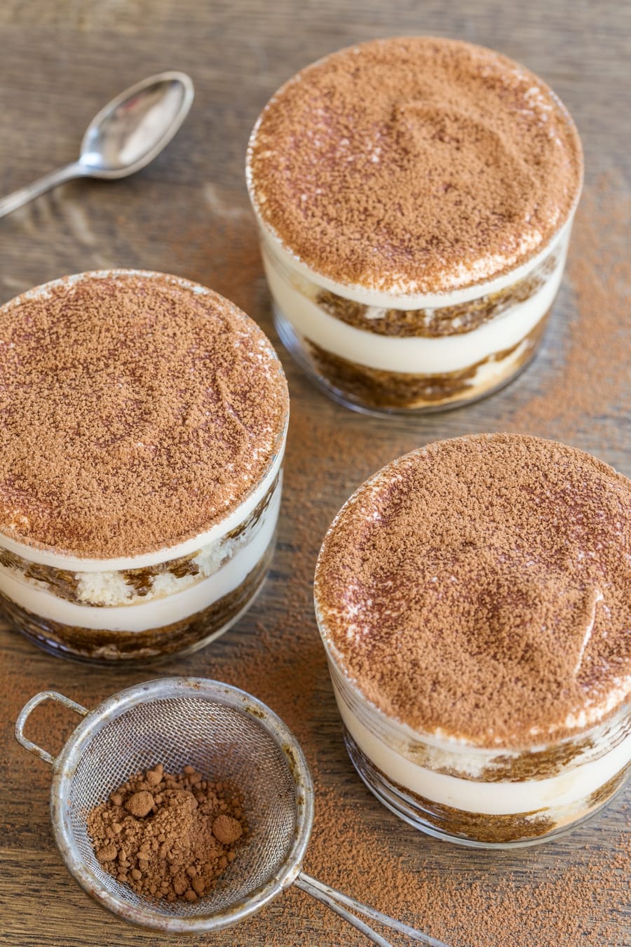 Dusting cocoa powder over tiramisu in a glass.